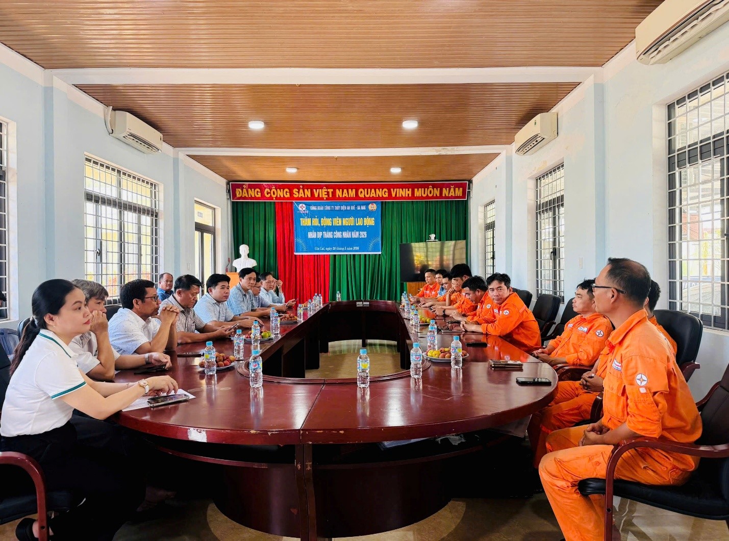 The image shows a group of people, presumably in a meeting, seated around a large, polished wooden table with a large, open room with high ceilings and decorations.AI-generated content may be incorrect.